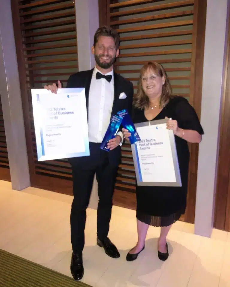 Man and woman dressed formally and smiling while holding framed certificates and trophies at the 2023 Telstra Best of Business Awards, representing Happiness Co as a winner.
