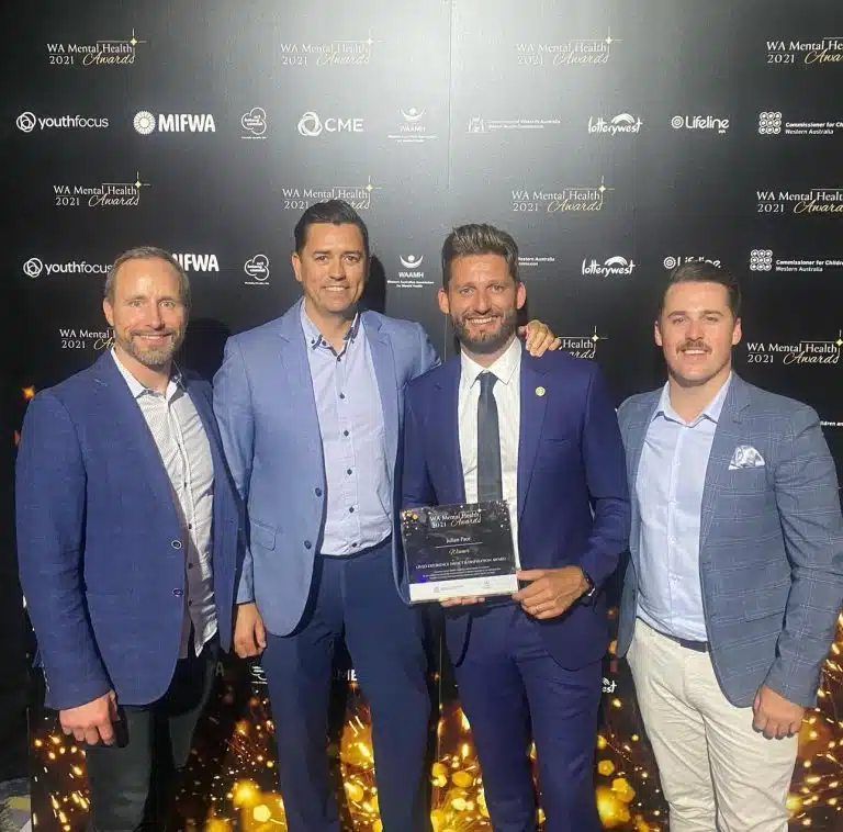 Four men in formal attire smiling with an award at the WA Mental Health Awards 2021 media wall